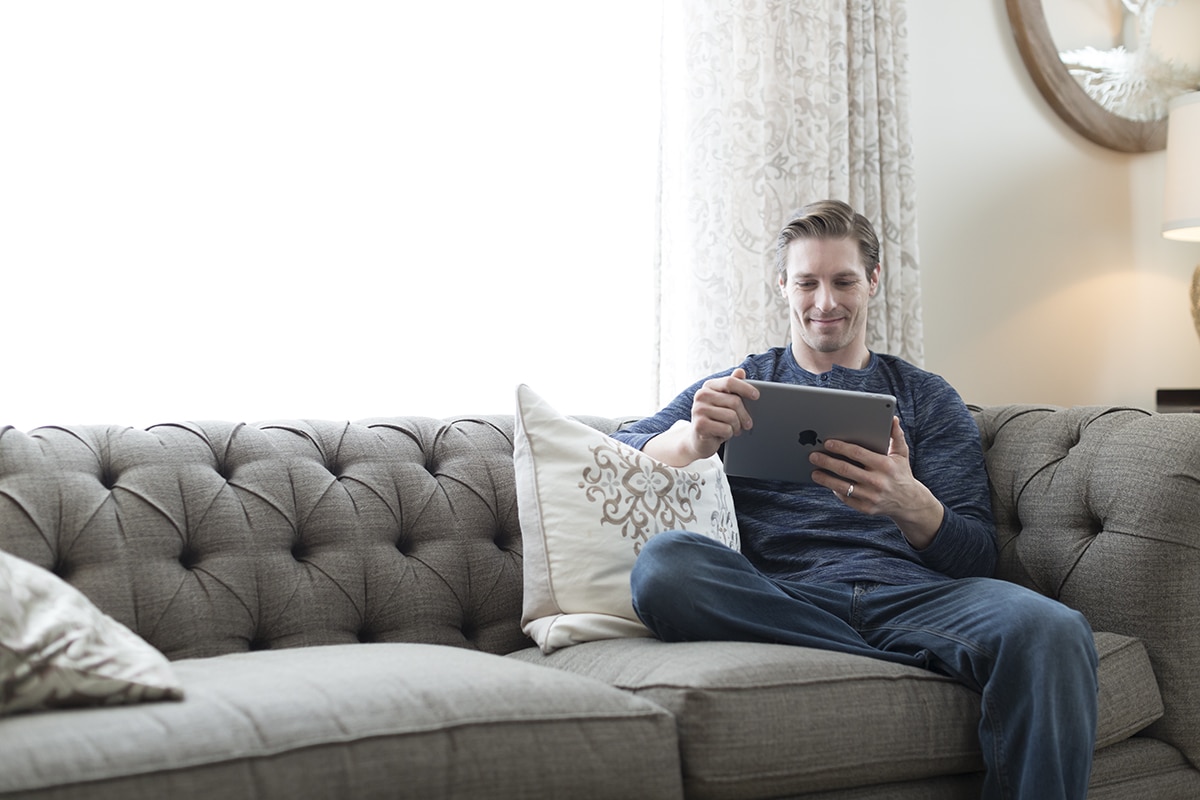 Man Sitting on a Large Spotless Gray Couch While Browsing on a Tablet